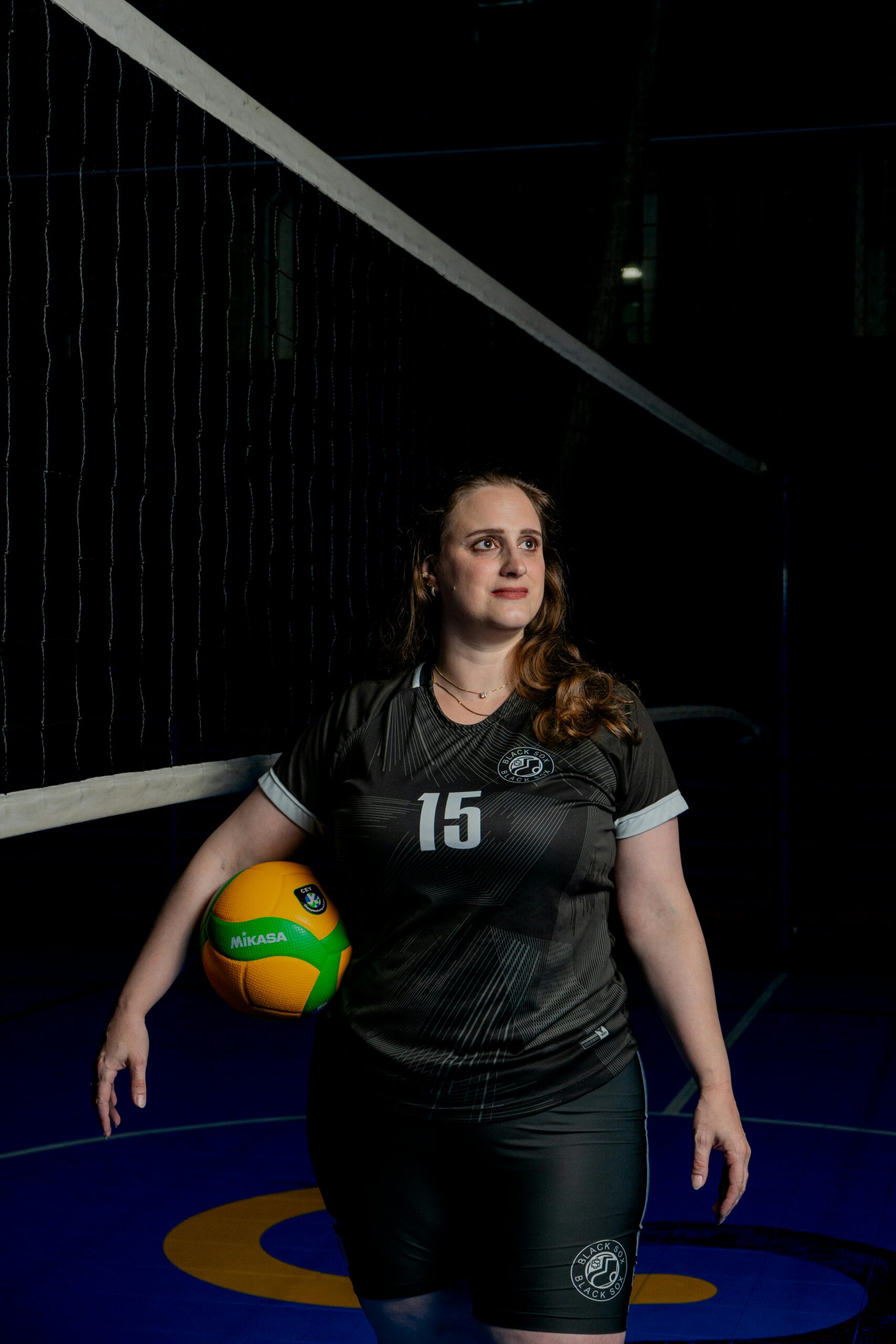 Focused female volleyball player standing on an indoor court with a ball, ready for the game.