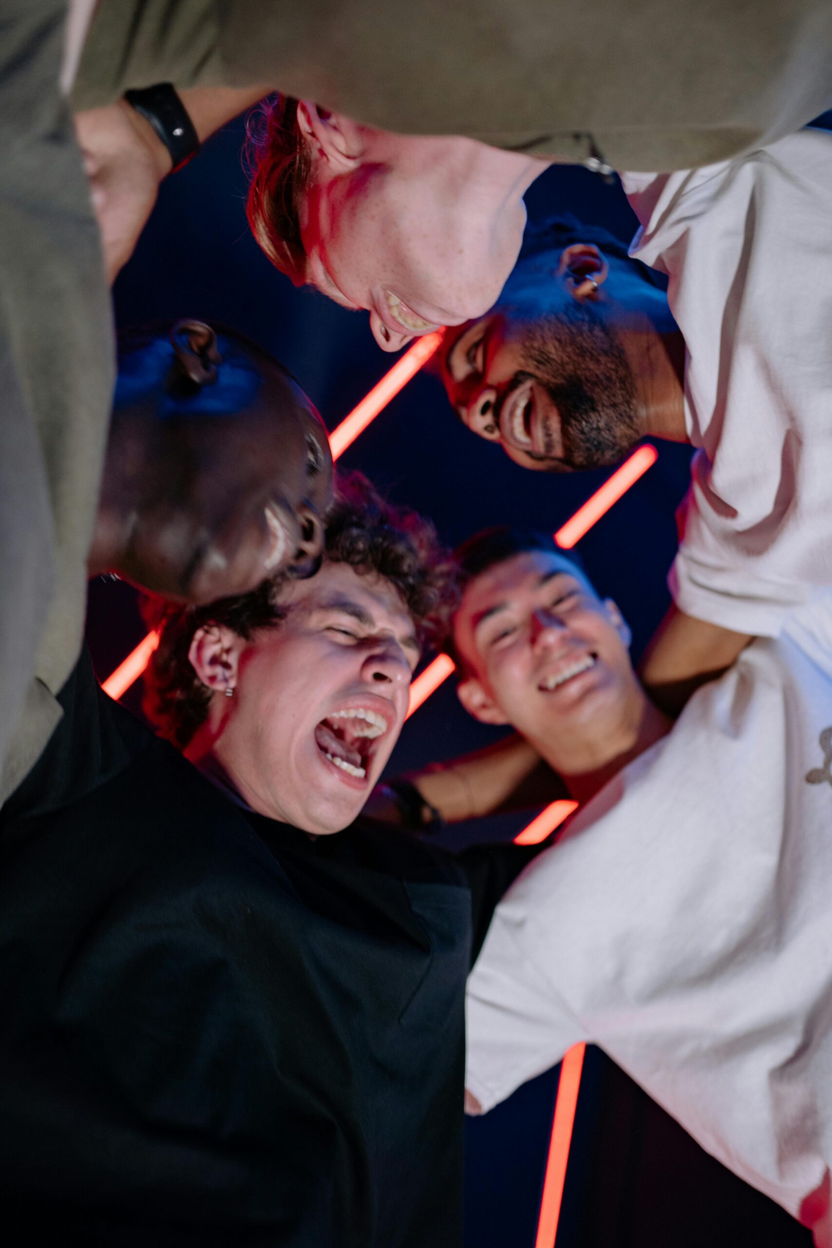 A diverse group of young adults joyfully huddling and celebrating under colorful lights.