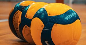 Close-up of three yellow and blue volleyballs aligned on an indoor court.