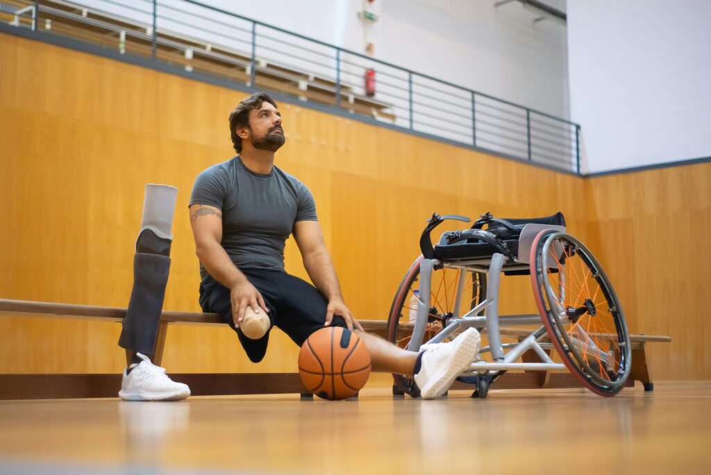 A man resting with a basketball and wheelchair in a gym setting, emphasizing adaptive sports.