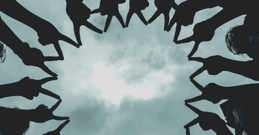 Silhouette of people forming a star with hands against a cloudy sky.