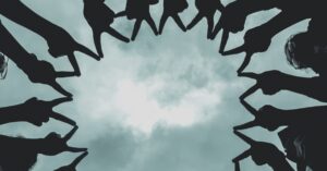 Silhouette of people forming a star with hands against a cloudy sky.
